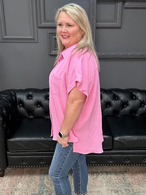 Woman in a pink shirt and blue jeans standing in front of a black leather couch.