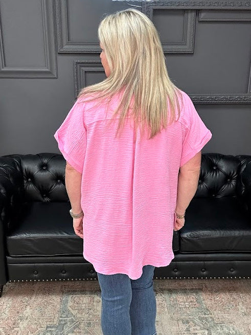 Person wearing a pink shirt and blue jeans standing in front of a black leather couch.