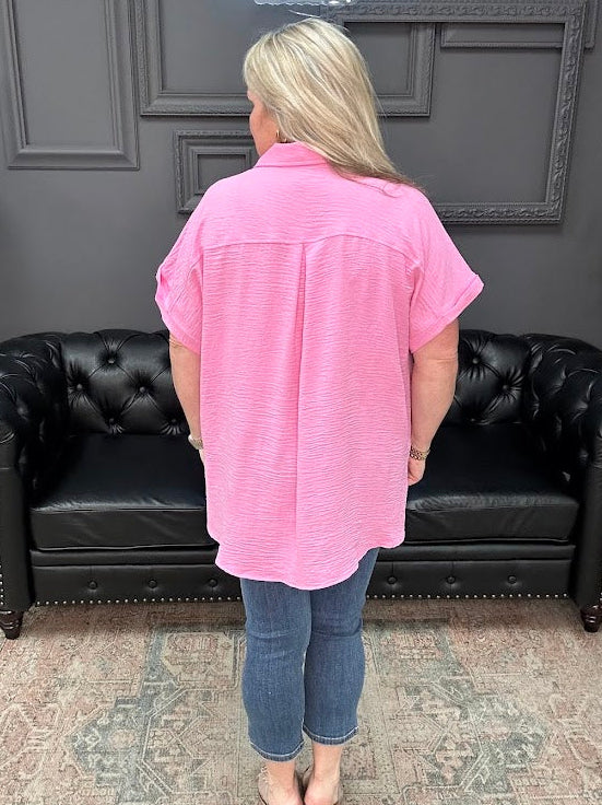 Person wearing a pink shirt and blue jeans standing in front of a black leather couch.