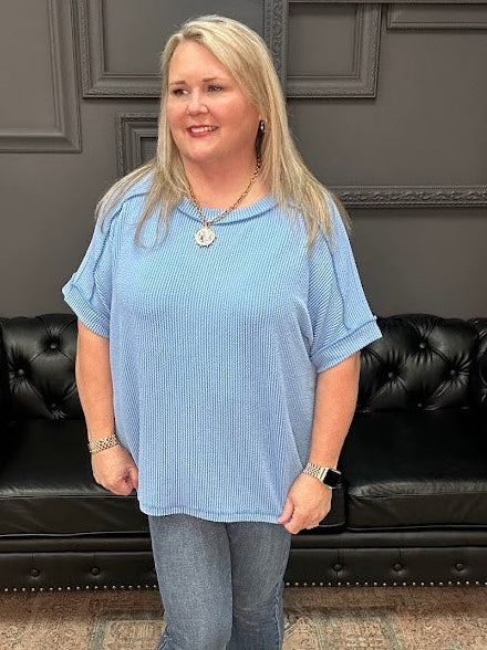 Woman in a blue shirt standing in front of a black leather couch with a dark wall and neon sign in the background.