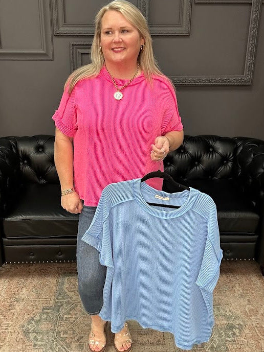 Woman holding a blue shirt in front of a black leather couch with a gray wall background.