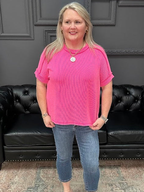 Woman in a pink shirt and blue jeans standing in front of a black leather couch.
