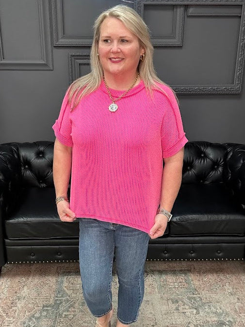 Woman in a pink shirt and blue jeans standing in front of a black leather couch.
