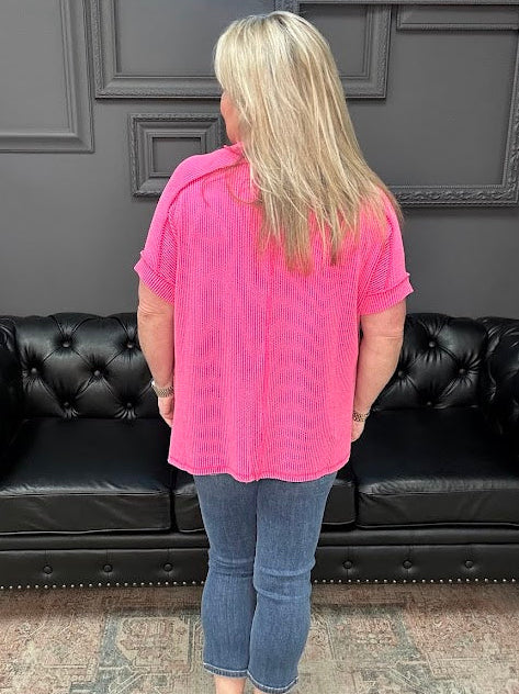 Person wearing a pink shirt and blue jeans standing in front of a black leather couch.