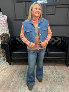 Woman wearing a denim vest and jeans standing in a room with a black leather couch and patterned rug.