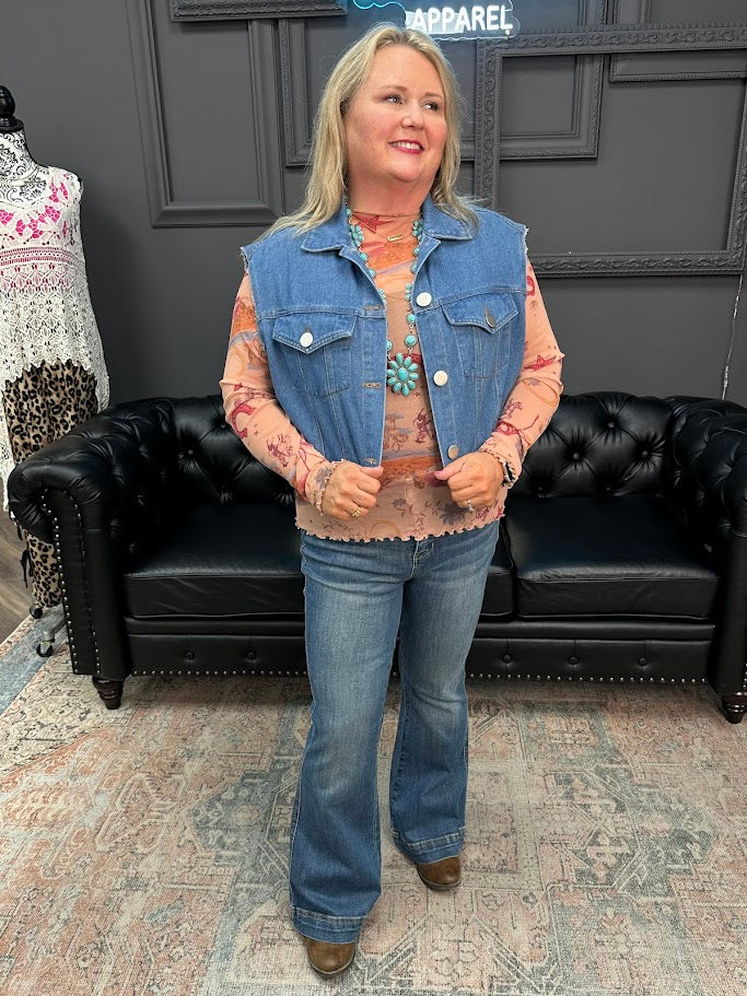 Woman wearing a denim vest and jeans standing in a room with a black leather couch and patterned rug.