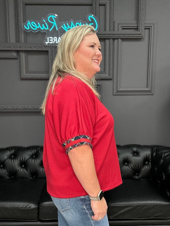Woman in a red top and blue jeans standing in a room with black leather couches and decorative wall.