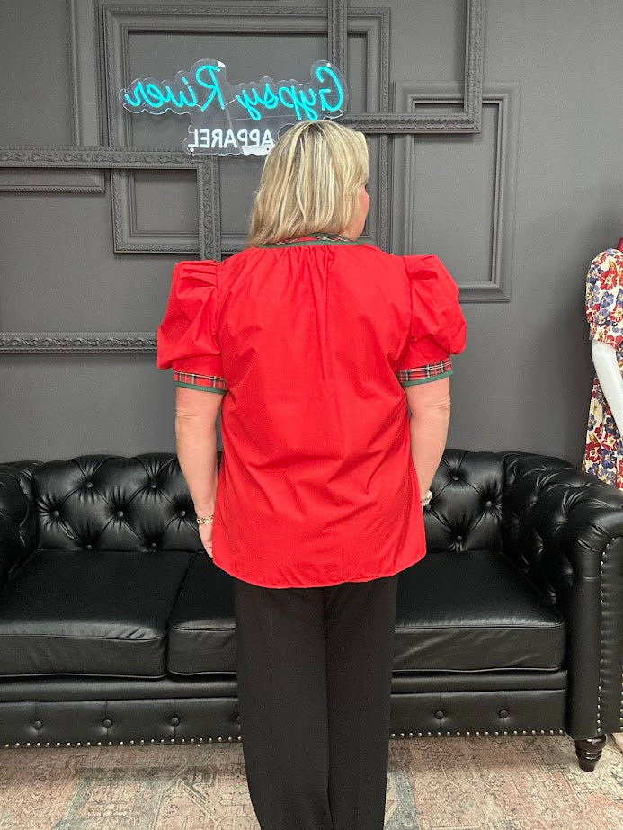 Person wearing a red blouse with puff sleeves in a room with a black couch and gray wall.
