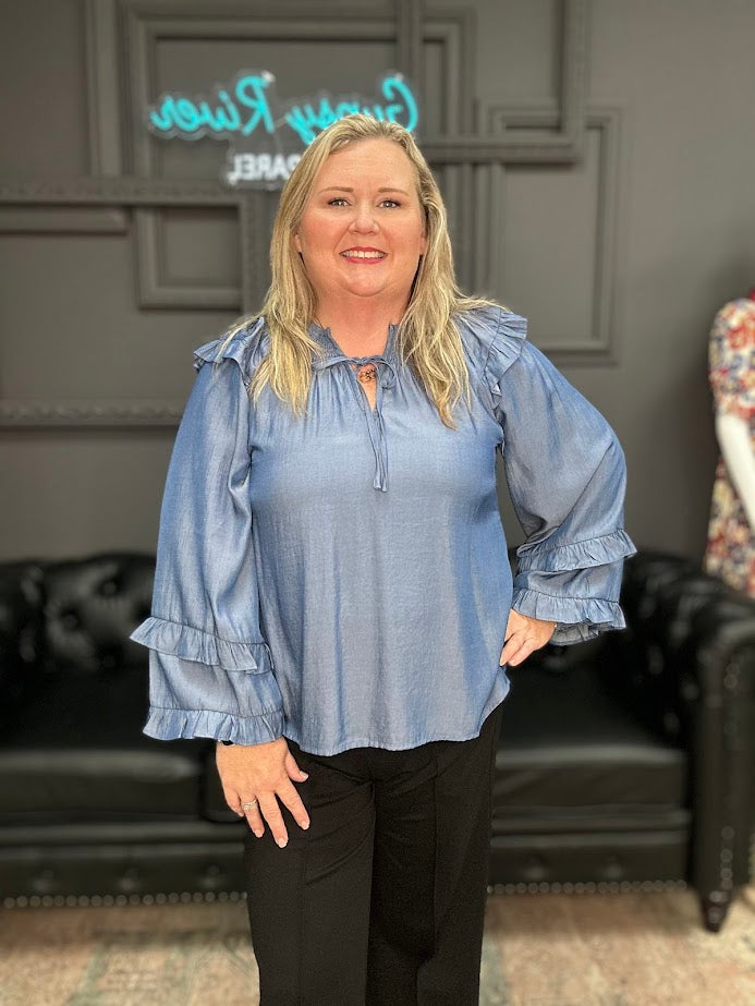Woman wearing a blue blouse with ruffled sleeves in an indoor setting.