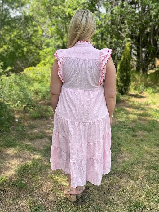 Woman wearing a pink dress standing in a grassy outdoor area with trees.