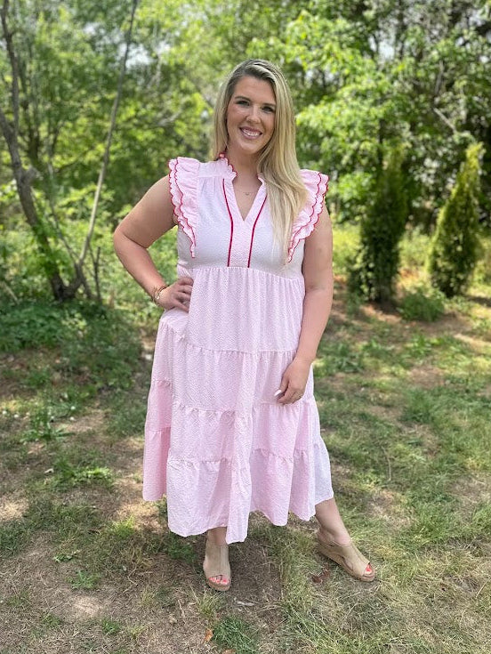 Woman in a pink dress standing outdoors with greenery in the background