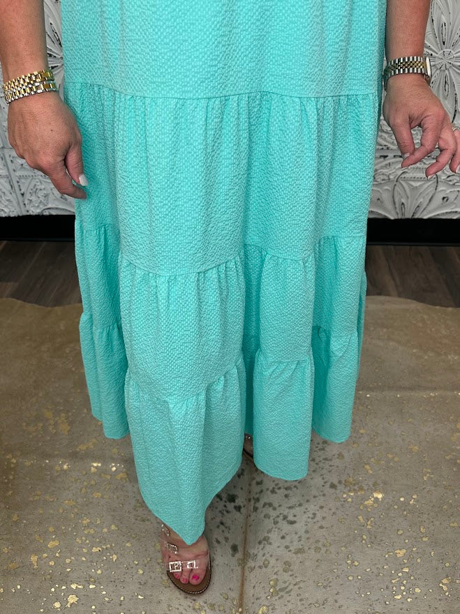 Teal dress with ruffled layers on a neutral background