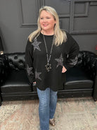 Woman wearing a black sweater with star patterns in a room with a black leather couch.