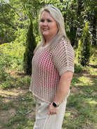 Woman standing outdoors in a natural setting wearing a beige crochet top and white pants.