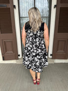 Woman wearing a black floral dress standing in front of a door.