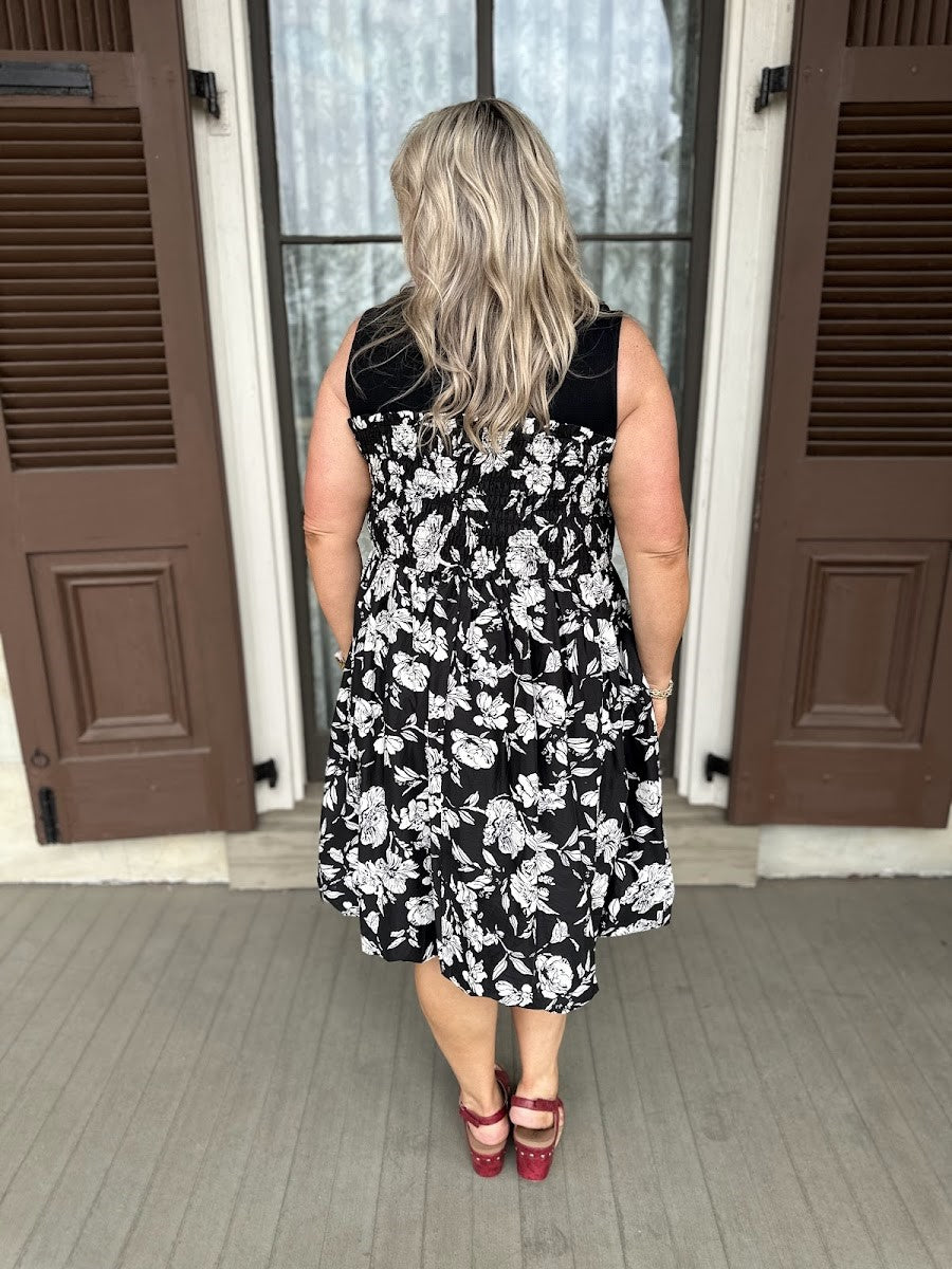 Woman wearing a black floral dress standing in front of a door.