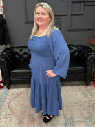 Woman in a blue dress standing in front of a Christmas tree and 'Gypsy River Apparel' sign.