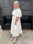 Woman in a white dress standing in a room with black leather couches and gray walls.