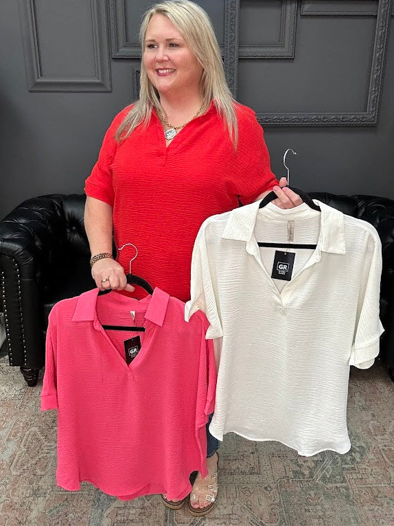 Woman holding two shirts, one pink and one white, in a store setting.