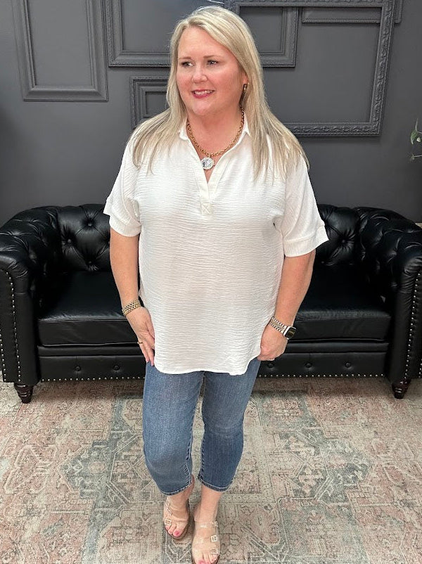 Woman in a white blouse and blue jeans standing in a room with a black leather couch and gray walls.