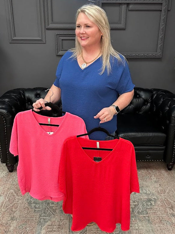 Woman holding two shirts, one pink and one red, in a store setting.