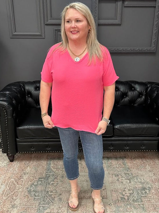 Woman in a pink shirt and jeans standing in front of a black leather couch.
