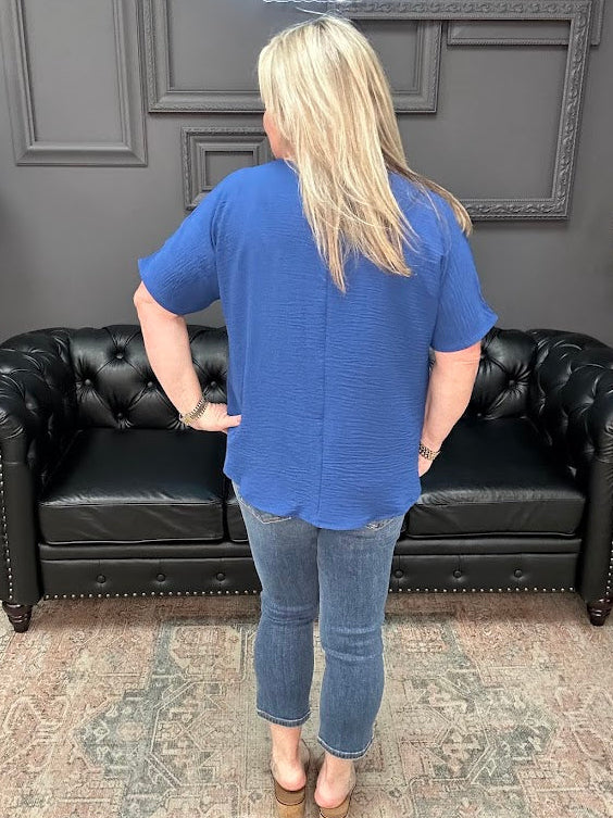 Person wearing a blue shirt and jeans standing in front of a black leather couch.