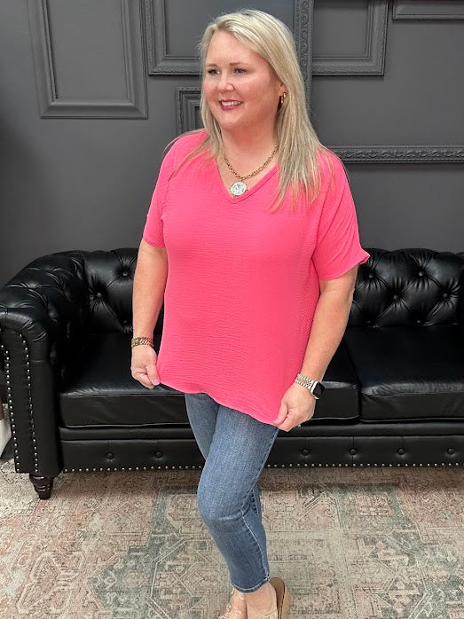 Woman in a pink shirt standing in front of a black leather couch with a gray wall and 'Apparel' sign in the background.