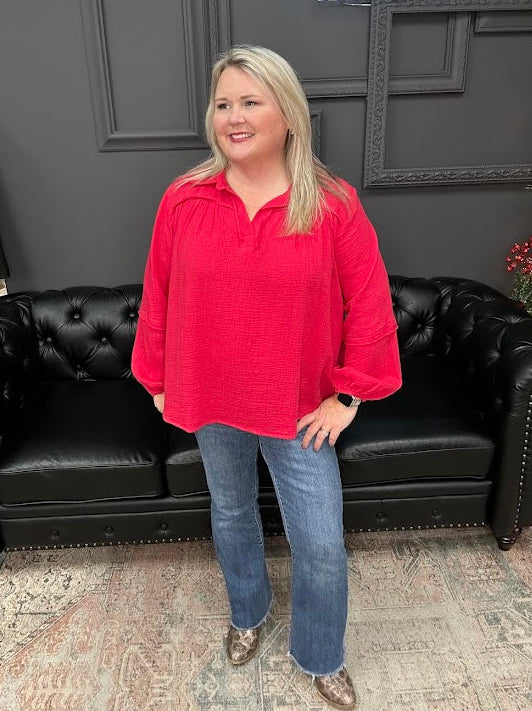 Woman in a red shirt and blue jeans standing in front of a black leather couch with 'Gypsy River Apparel' branding.