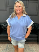 Woman wearing a light blue polo shirt with white trim in an indoor setting.