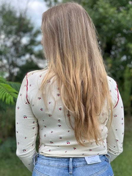 Person wearing a white blouse with floral patterns and blue jeans in an outdoor setting.