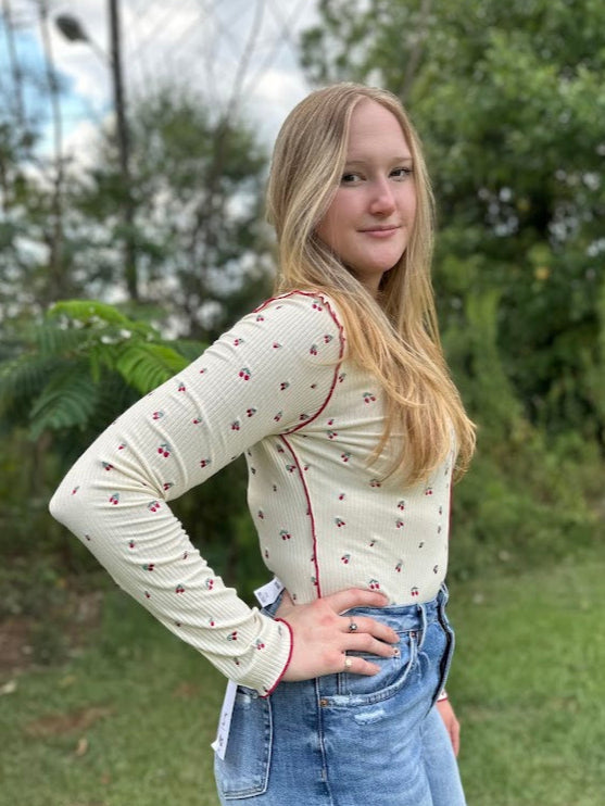 Woman wearing a cream long-sleeve top with red trim and blue jeans outdoors.