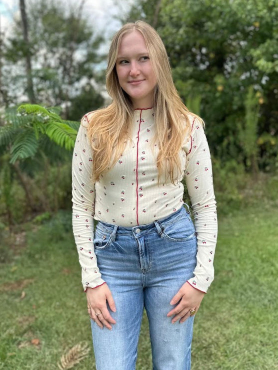 Woman wearing a white blouse with red accents and blue jeans standing outdoors.