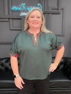 Woman wearing a green blouse with red accents in a room with black leather couches and decorative wall.