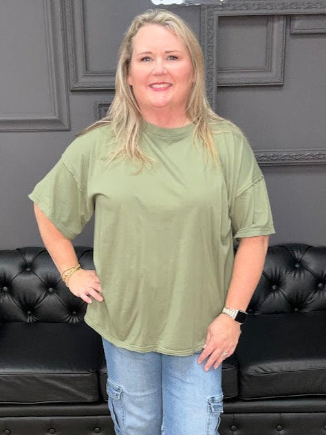 Woman wearing a green oversized shirt and blue jeans standing in a room with black leather furniture.