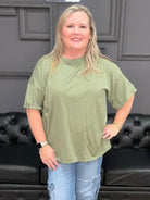 Woman wearing a green oversized shirt and blue jeans standing in a room with black leather furniture.