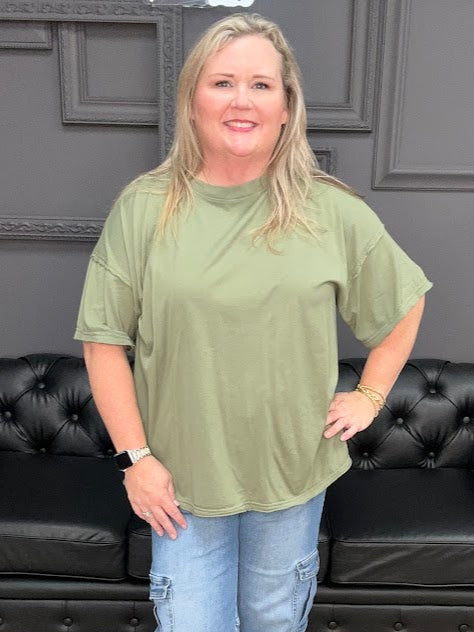 Woman wearing a green oversized shirt and blue jeans standing in a room with black leather furniture.